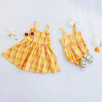 Yellow plaid dress and romper set on a light gray background with decorative items.