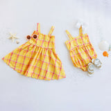 Yellow plaid dress and romper set on a light gray background with decorative items.