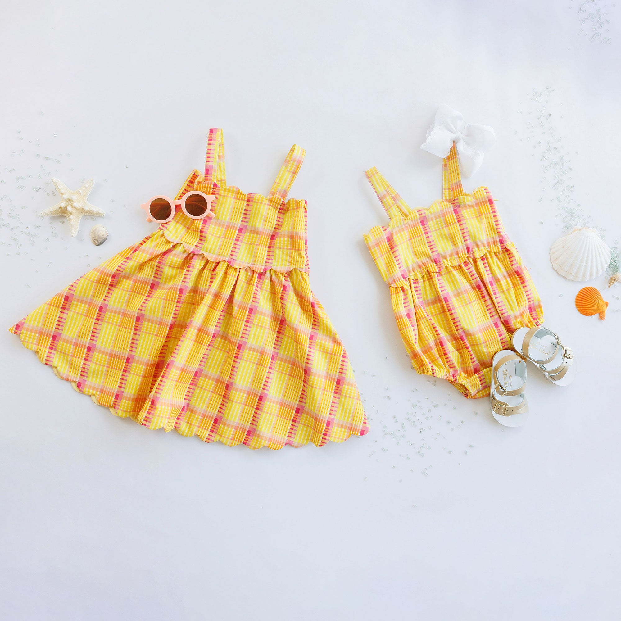 Yellow plaid dress and romper set on a light gray background with decorative items.