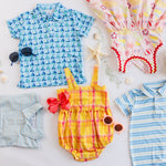 Collection of children's clothing including a blue patterned shirt, yellow and pink romper, and striped shirt on a light background.