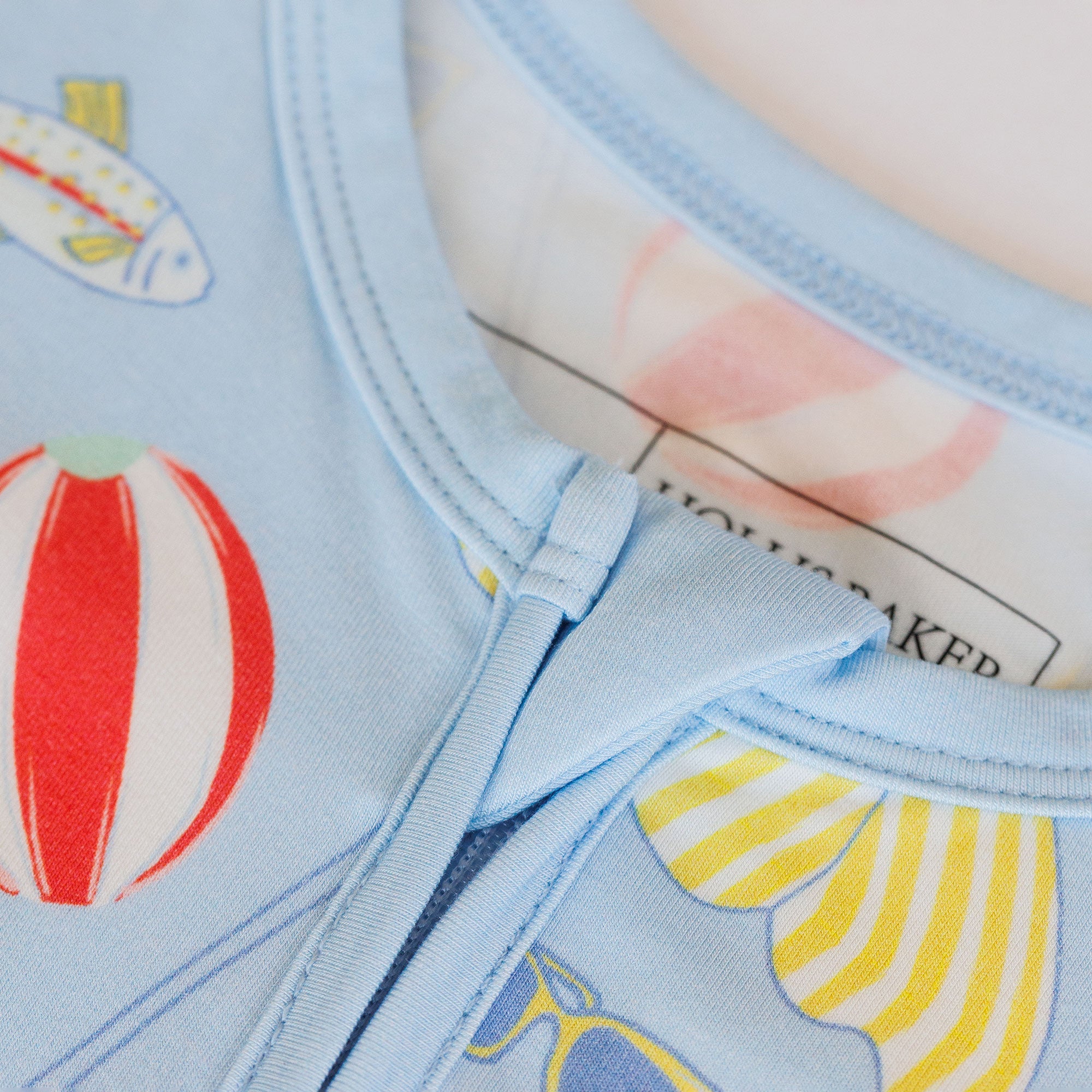 Close-up of a light blue fabric with colorful patterns including a red and white striped balloon and yellow and white striped sailboat.