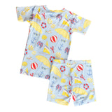 Children's loungewear set with a blue pattern featuring yellow umbrellas, red life buoys, and white clouds on a light beige background.