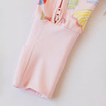 Pink children's zipper romper with colorful shell designs on a light gray background