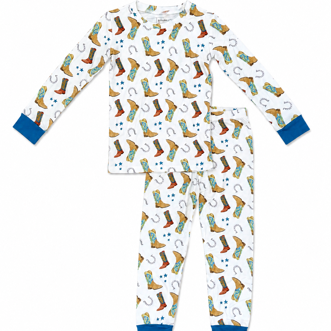 A two-piece children's pajama set featuring a white long-sleeve top and matching pants with a colorful cowboy boots and horseshoe pattern, finished with solid blue cuffs and ankles.